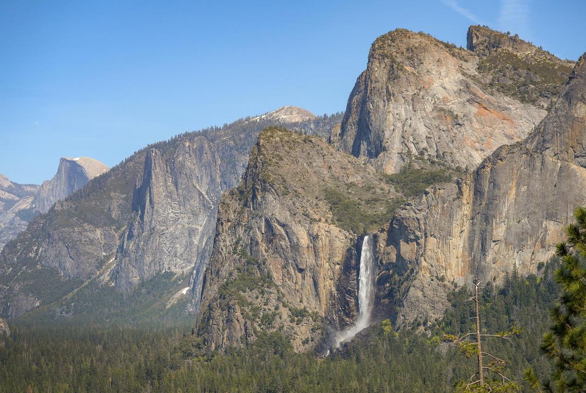 Half Dome comes into view at left while water rushes over Bridalveil Fall in Yosemite Valley in spring at Tunnel View in Yosemite National Park on Friday, April 23, 2021.