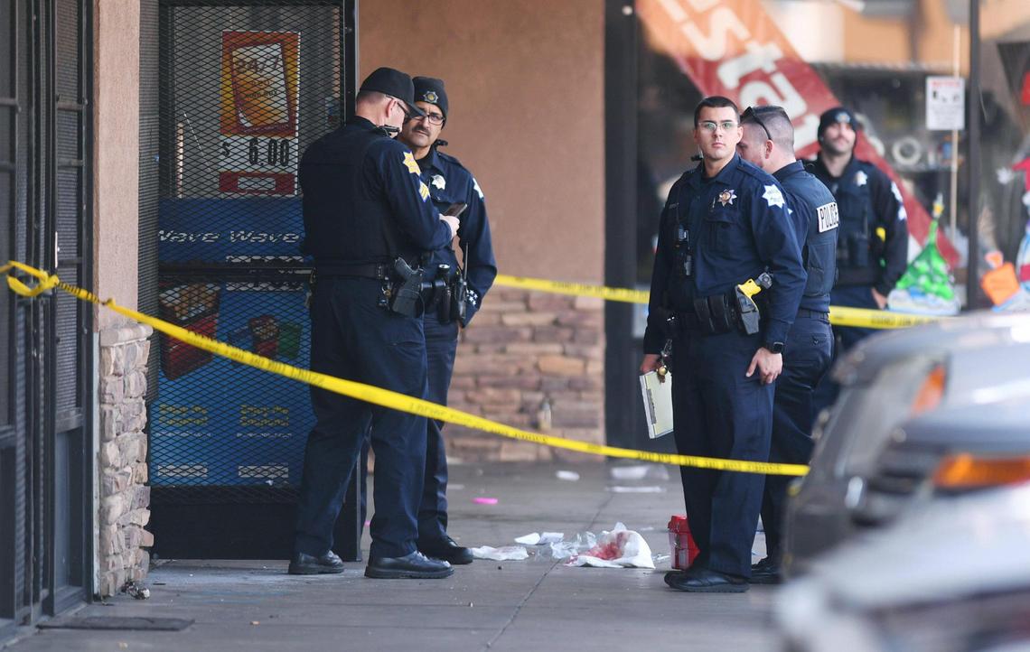 Fresno police stand outside a smoke shop as they investigate a double homicide in the Princeton Square strip mall at Blackstone and Princeton avenues on Wednesday, Dec. 14, 2022 in Fresno.