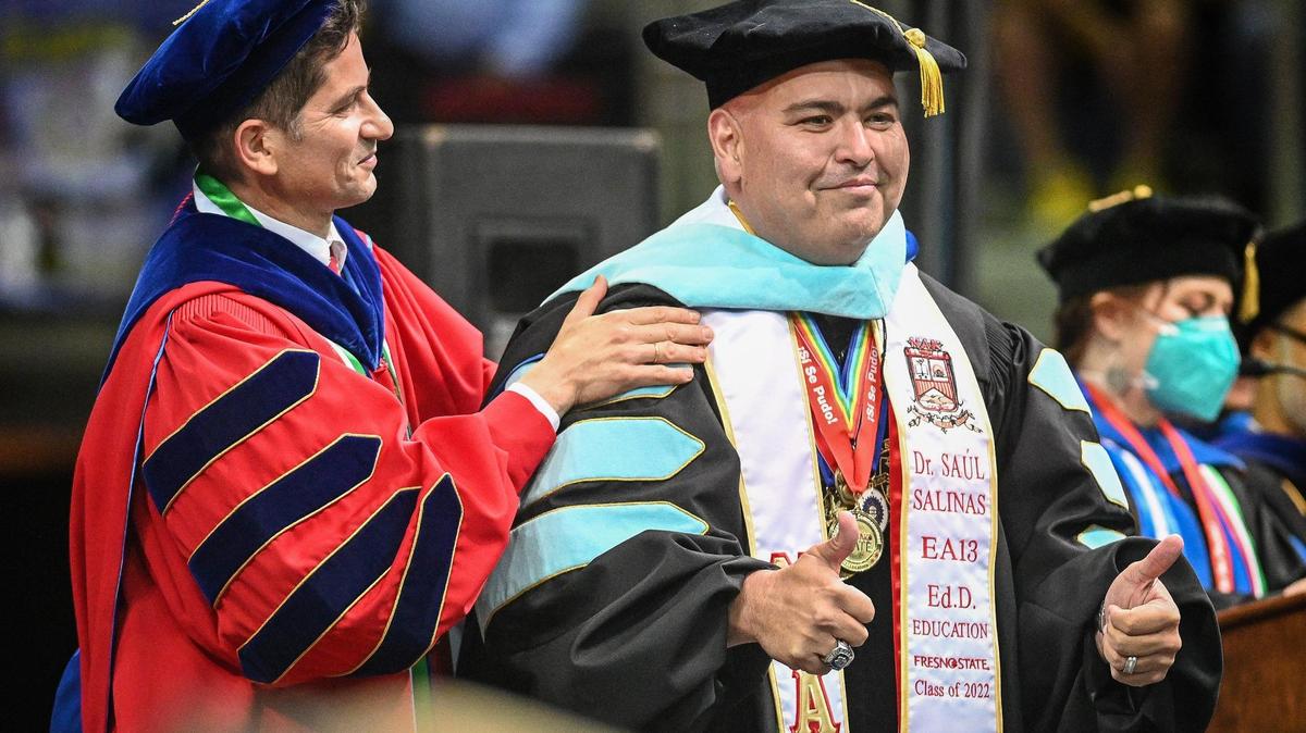 Saúl Salinas muestra los dos pulgares hacia arriba mientras es felicitado por obtener su doctorado por el presidente de Fresno State, Saúl Jiménez Sandoval, durante la 46ª ceremonia de graduación  chicana/latina anual de Fresno State celebrada en el Save Mart Center, el sábado 21 de mayo de 2022.