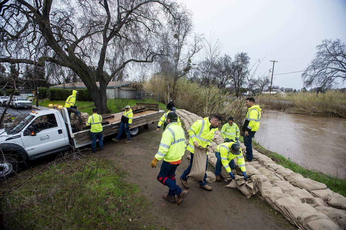 City of Merced Public Works employees construct a sandbag wall along Bear Creek near the intersection of W Street and West 23rd Street in Merced, Calif., on Wednesday, Jan. 11, 2023.