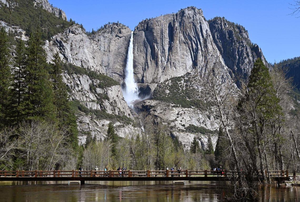 Visitors walk along Swinging Bridge viewing Upper Yosemite Falls and the rising Merced River on Friday, April 28, 2023, in Yosemite Valley. Park officials expect the Merced River to continue rising due to snow melt.