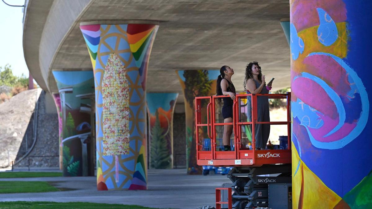 Assistant Eden Santos, left, stands next to. muralist Andrea Cano Torres as they assess a mural depicting US poet laureate and writer Juan Felipe Ferrera on a support column underneath Highway 180 at San Pablo Park Thursday, July 17, 2025 in Fresno. The murals by several artists are a collabortion between the Fresno Arts Council and Caltrans, said muralist ANdrea Cano Torres.