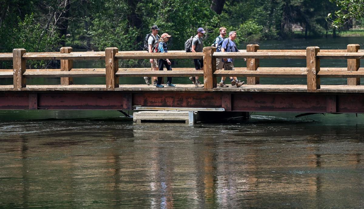 Yosemite National Park visitors cross the bridge which barely clears the water level on the Merced River at the Swinging Bridge picnic area in Yosemite Valley on Tuesday, June 13, 2023.