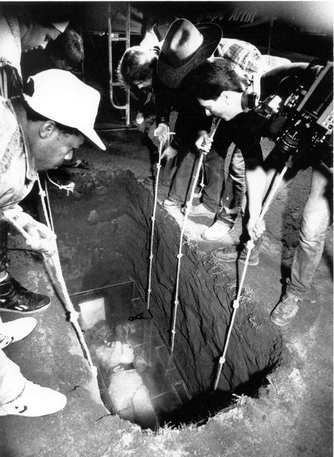 Using ropes, workers lower Joe Burrus and plastic coffin.