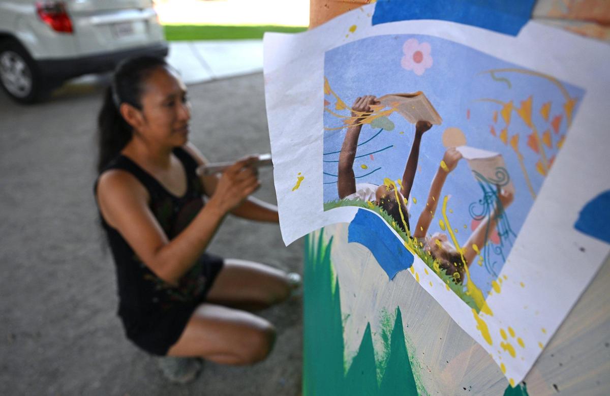 Eden Santos, assisting muralist Andrea Cano Torres, works on a mural titled Through Words, Dreams Are Born, on support pillars underneath Highway 180 at San Pablo Park Thursday, July 17, 2025 in Fresno. The murals by several artists are a collabortion between the Fresno Arts Council and Caltrans, said muralist ANdrea Cano Torres.