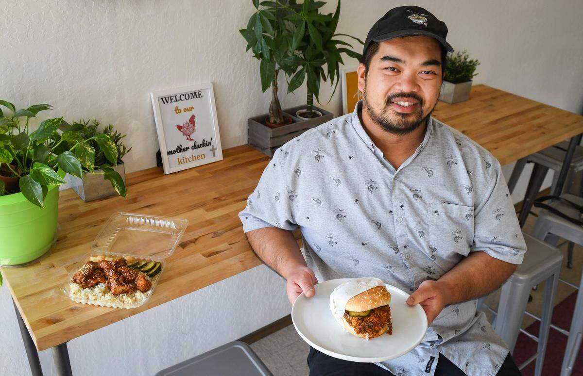 Long Nguyen, owner of Pacific Fried Chicken, sits with a hot chicken sandwich with homemade pickles and slaw and a garlic-scallion rice bowl with boneless Asian wings at his restaurant which recently opened last summer in southeast Fresno.