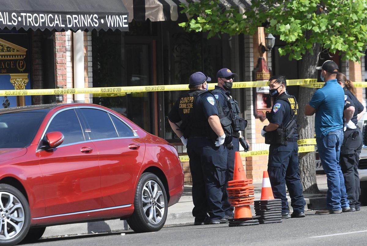 At the scene of an early-morning shooting that left two dead and one wounded, Clovis Police officers confer near a red Mercedes, doors secured with crime scene stickers, that was later towed from in front of The Palace bar at 446 Clovis Ave. on Saturday morning, May 22, 2021.