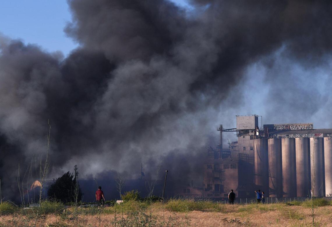 Three people watch as smoke rises from a warehouse fire on North Thorne Avenue, just north of West Nielsen Avenue, on Saturday, June 26, 2021.