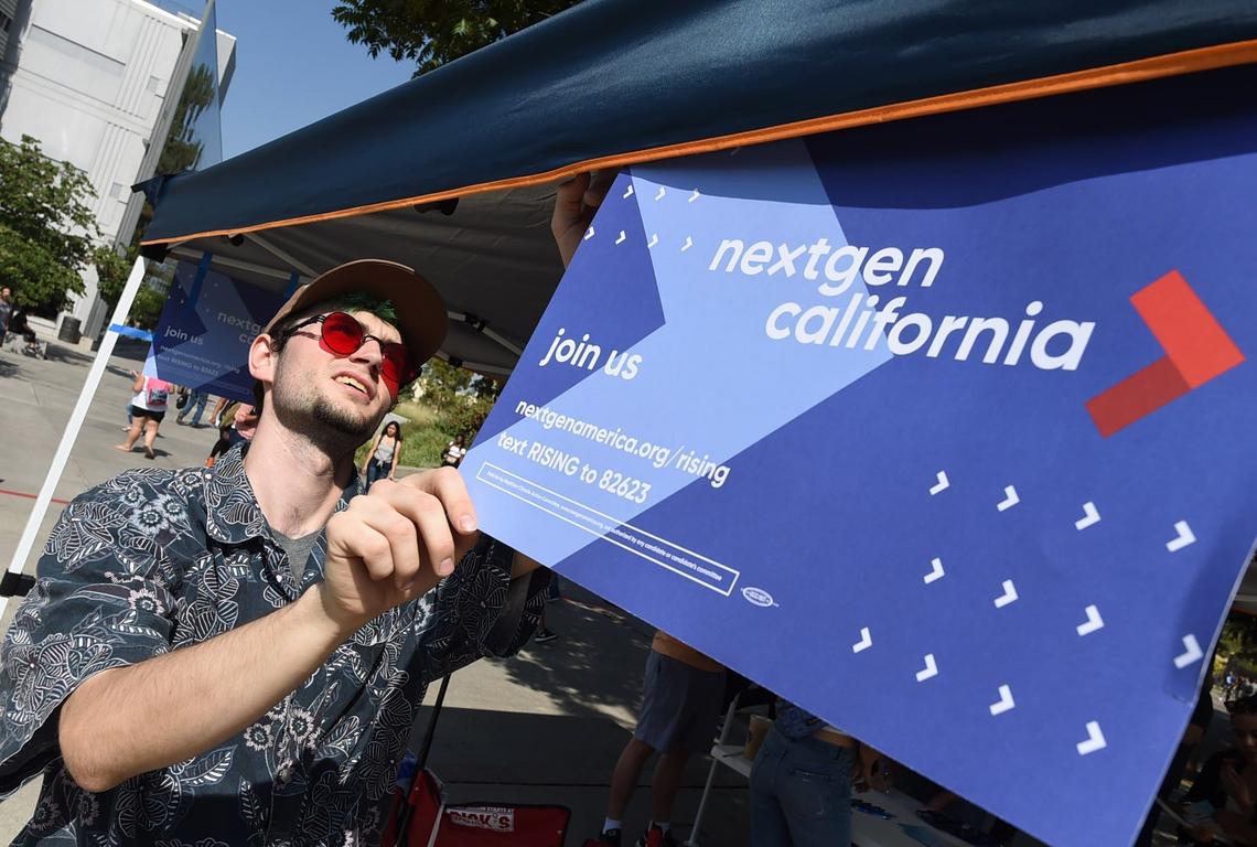 NextGen America volunteer Kris Hall puts up a sign on the group’s booth on the first day of classes at Fresno State, Thursday morning, Aug. 23, 2018.