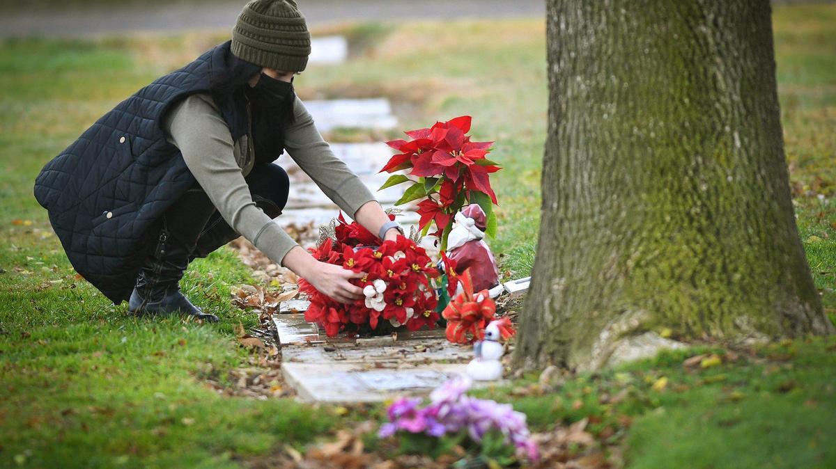 At the base of a large tree at the Chowchilla Cemetery, Sarah Rodriguez tends to the grave of her cousin Calley Jean Garay, decorated for the holidays on Dec. 31, 2020. Calley was killed, allegedly by her husband, outside a clinic in Madera in July.