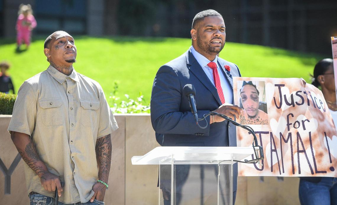 Jamal Jones, left, looks skyward while his lawyer Rodney Diggs holds a sign with a photo showing Jones’ injuries after a traffic stop in Clovis last year, during a news conference to announce a lawsuit with be filed against the Clovis Police Department, accusing the department of racial profiling, excessive force and severe injury from a police canine, outside the Robert E Coyle Federal Building in downtown Fresno on Thursday, April 28, 2022.