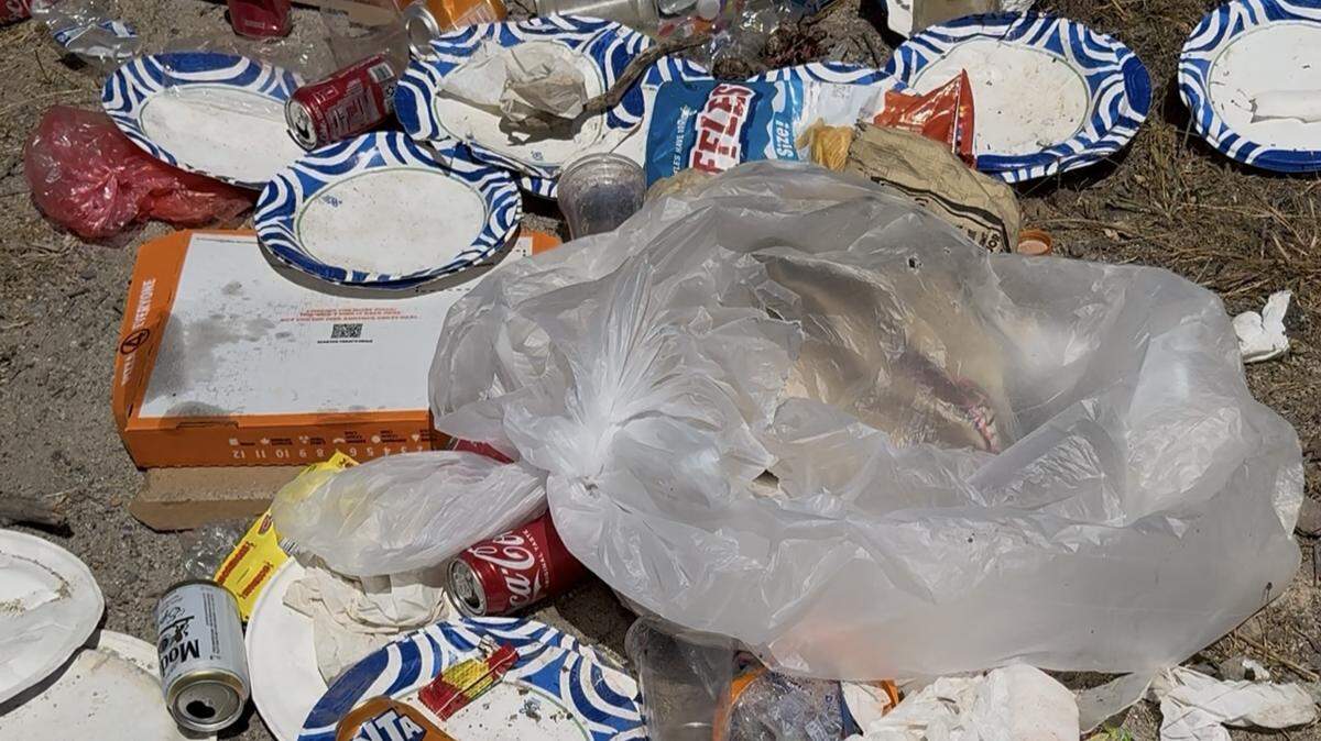 Paper plates, plastic bags, aluminum cans and pizza boxes lay strewn on the ground near the shoreline of Bass Lake in Madera County following the Fourth of July weekend in 2025.