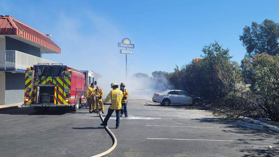 Fire crews work to extinguish flames from a grass fire that spread into the parking lot of a Days Inn, set four vehicles ablaze and left two people hospitalized Sunday, May 30, 2021, in Fresno, California.