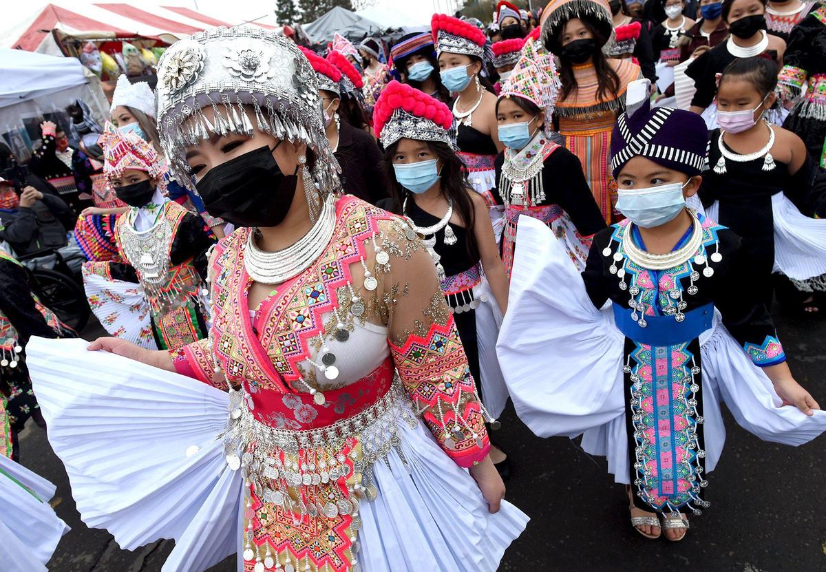 Masked up, 18-year-old Krystal Vue, left, is mimicked by younger dancers, including Helena Vang, 7, right, as they march in the opening day parade ushering in the Hmong New Year celebration at the Fresno Fairgrounds, Thursday morning, December 30, 2021. They are members of the Hmong Cultural and Arts Preservation group.