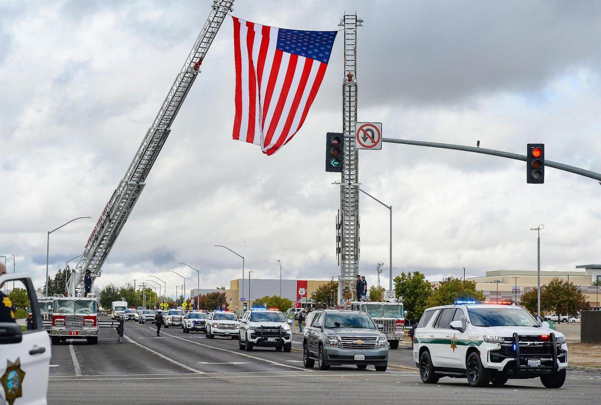 Fresno County Sheriff’s Office officers lead a motorcade below an American flag lifted by Fresno Fire Department ladder trucks following a memorial service for Toamalama Scanlan at the Save Mart Center in Fresno on Monday, Oct. 25, 2021.