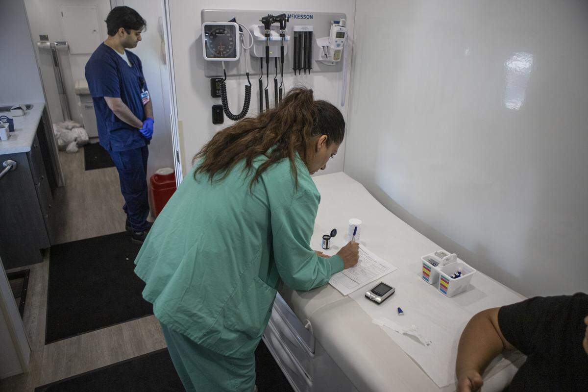 Dr. Navdeep Lehga checks a patient’s blood sugar in the exam room of the Saint Agnes Mobile Health Unit clinic, parked in the lot of Rojas Pierce Park in Mendota on Aug. 28, 2025. Photo by Larry Valenzuela, CalMatters/CatchLight Local