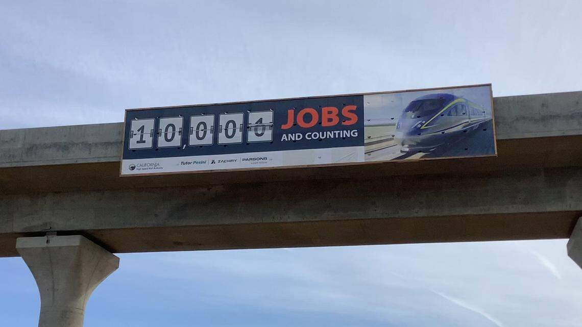 A sign affixed to the structure of a high-speed rail viaduct over Cedar Avenue near Highway 99 in south Fresno on Tuesday, Feb. 14, 2023, boasts the California High-Speed Rail Authority reaching a milestone of creating 10,000 jobs for construction of the project in the San Joaquin Valley.