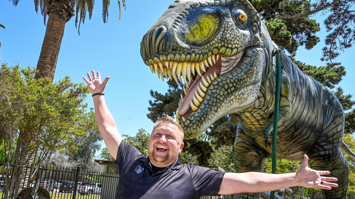 Davey Helm of Helm and Sons Amusements poses with his T-rex at the entrance to Playland in Roeding Park, which has been promised to reopen on June 1.