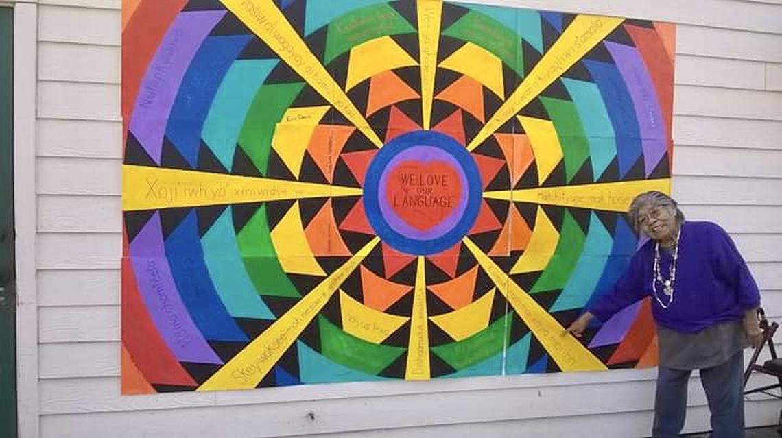 Marie Wilcox beside a mural promoting the preservation of indigenous languages.