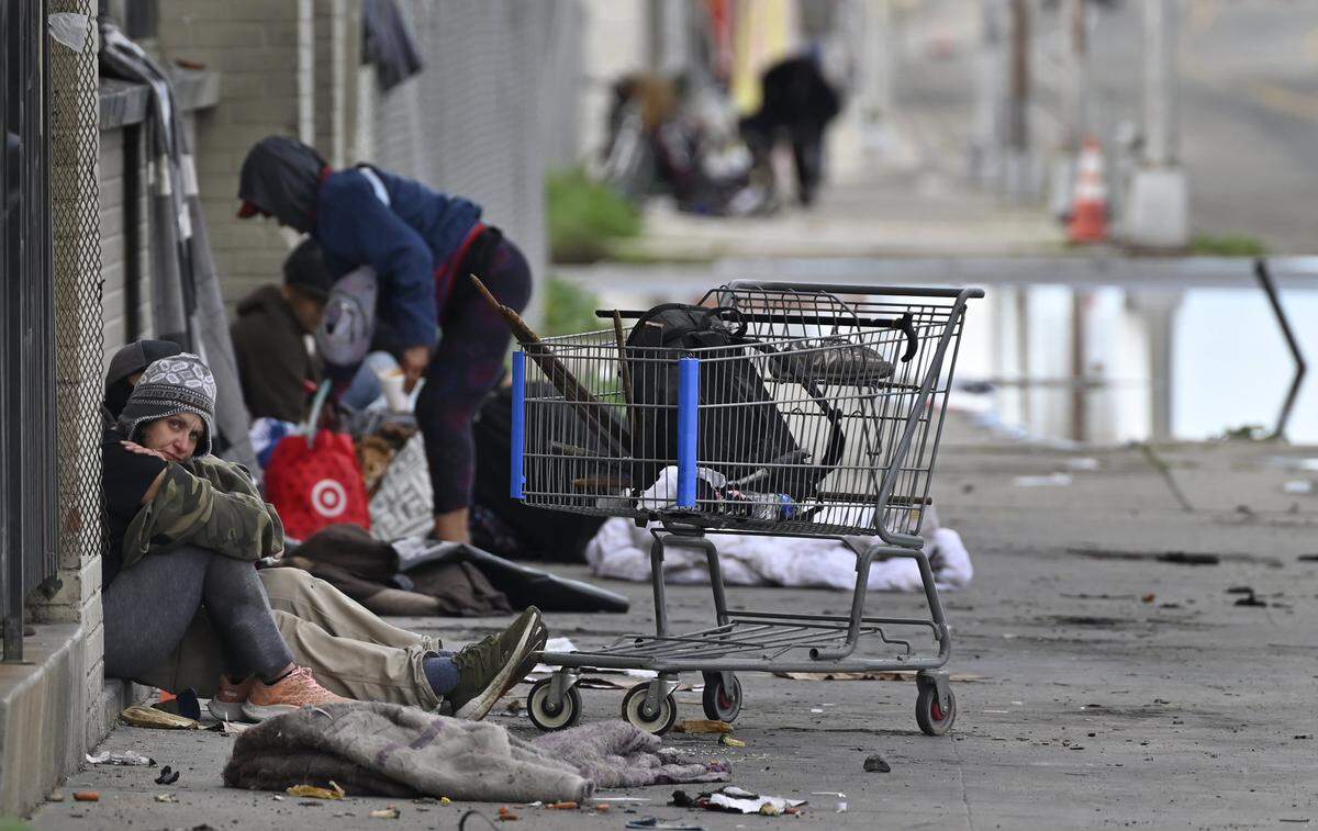 A woman stares as homeless gather on a sidewalk along G Street Friday, Dec. 26, 2025 in downtown Fresno.