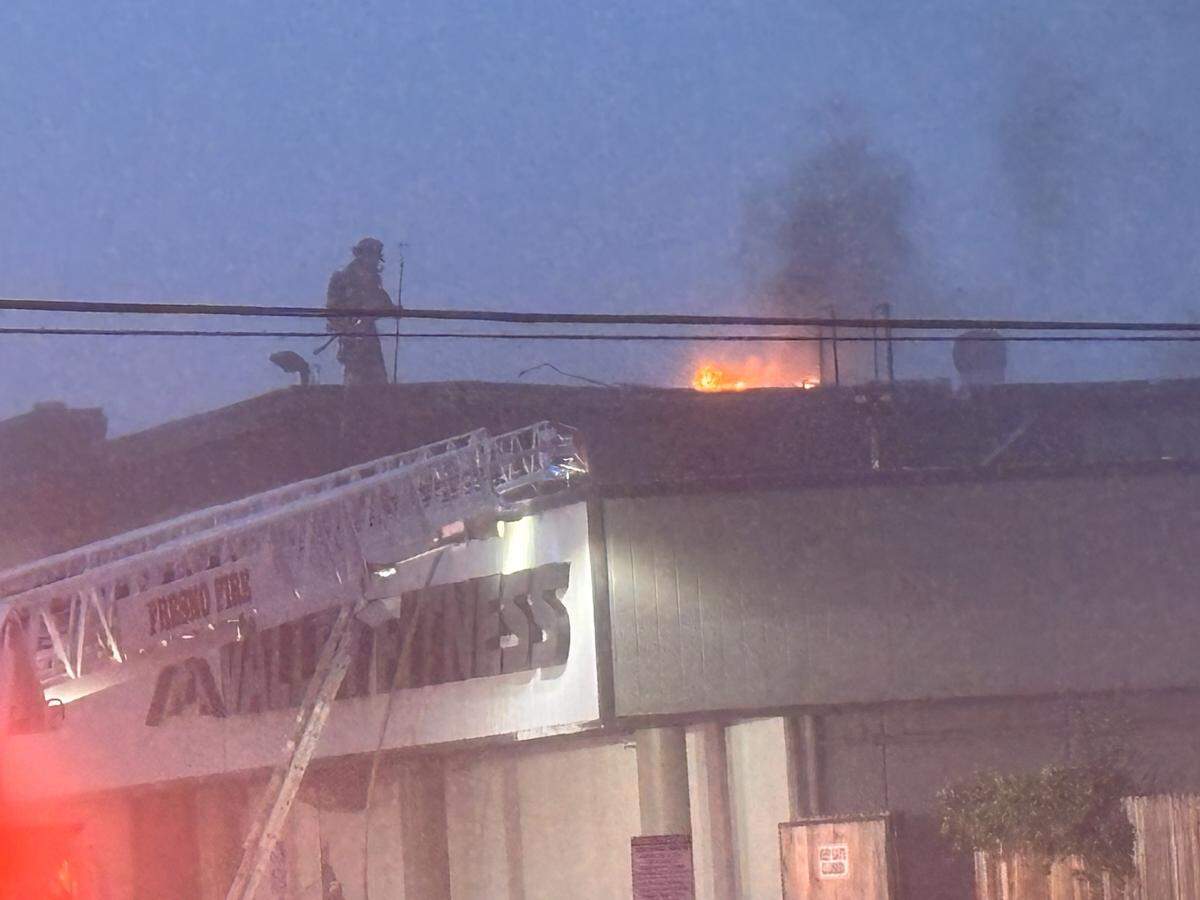 A firefighter works to extinguish a fire on top of Valley Fitness Center on Maroa Avenue near Shields Avenue on Tuesday, Dec. 30, 2025.