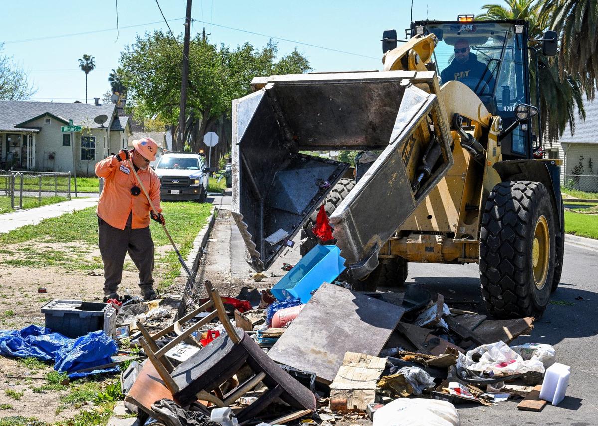 A city worker rakes up small bits of debris while another uses “the Claw” frontloader to scoop up residential trash left out on a street in southeast Fresno during Operation Cleanup in Fresno on Monday, April 8, 2024.