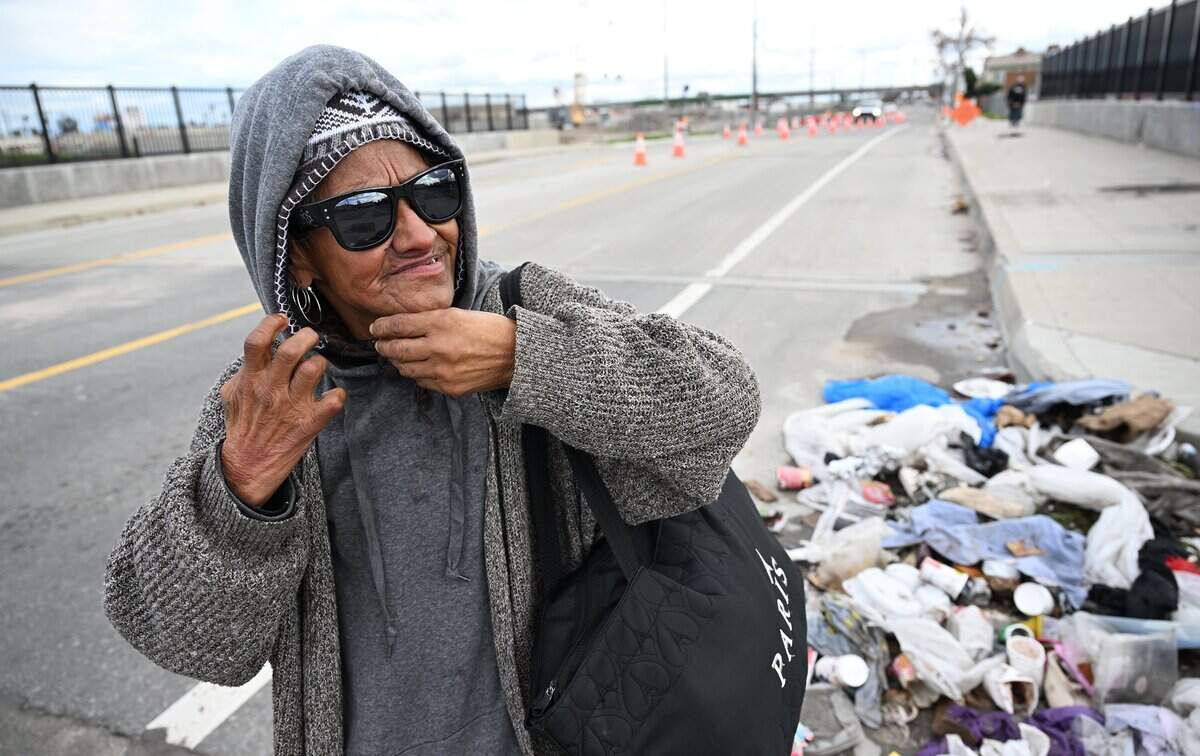 A homeless woman fixes her earring as she passes a pile of refuse along G Street Friday, Dec 26, 2025 in downtown Fresno.