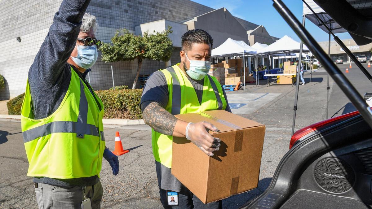 Richard Ramirez-Ghimenti, left and Christian Gonzalez, both from Centro La Familia, help load a box of food into a car during a food distribution event outside The Fresno Center in southeast Fresno on Tuesday, Nov. 10, 2020. The Fresno County Health Department has been utilizing community health workers to educate residents in poorer areas to help fight the coronavirus pandemic. Over 20 nonprofits have joined to train community health workers using CARES dollars.