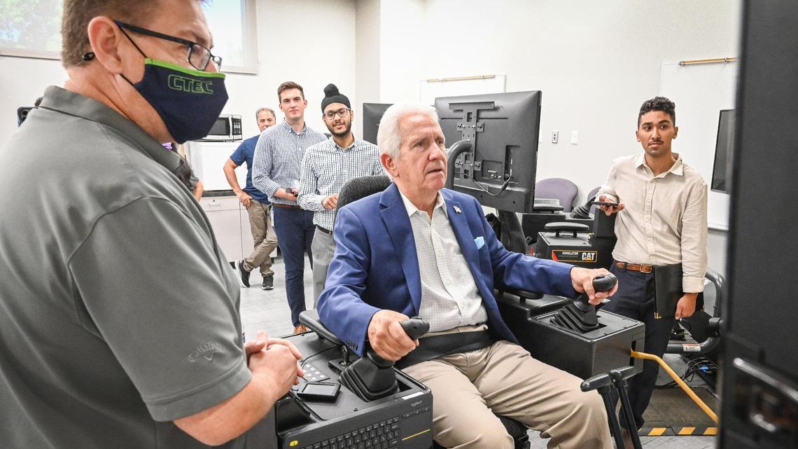 Congressman Jim Costa tries out a heavy equipment simulator with the help of CTEC High School instructor Brian Emerson, left, after announcing new funding of $23 million through the American Rescue Plan Good Jobs Challenge awarded to the Fresno County Economic Development Corporation to develop and launch the project, at CTEC High School in Fresno on Thursday, Aug. 4, 2022.