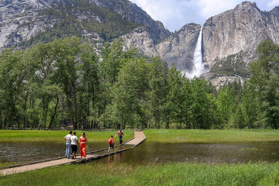 Visitantes de Yosemite National Park contemplan cruzar una pasarela inundada en un prado frente a Upper Yosemite Falls en Yosemite Valley el martes 13 de junio de 2023.
