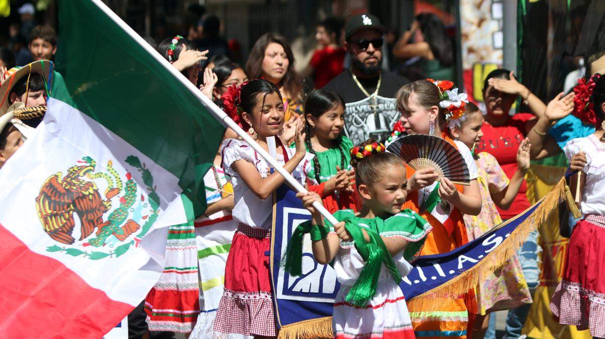 A folklórico dancer  waves the Mexican flag during the Fiestas Patrias parade at the Fulton Mall on Sept. 15, 2024. / Una danzante folklórica ondea la bandera mexicana durante el desfile de las Fiestas Patrias en el Fulton Mall el 15 de septiembre de 2024.