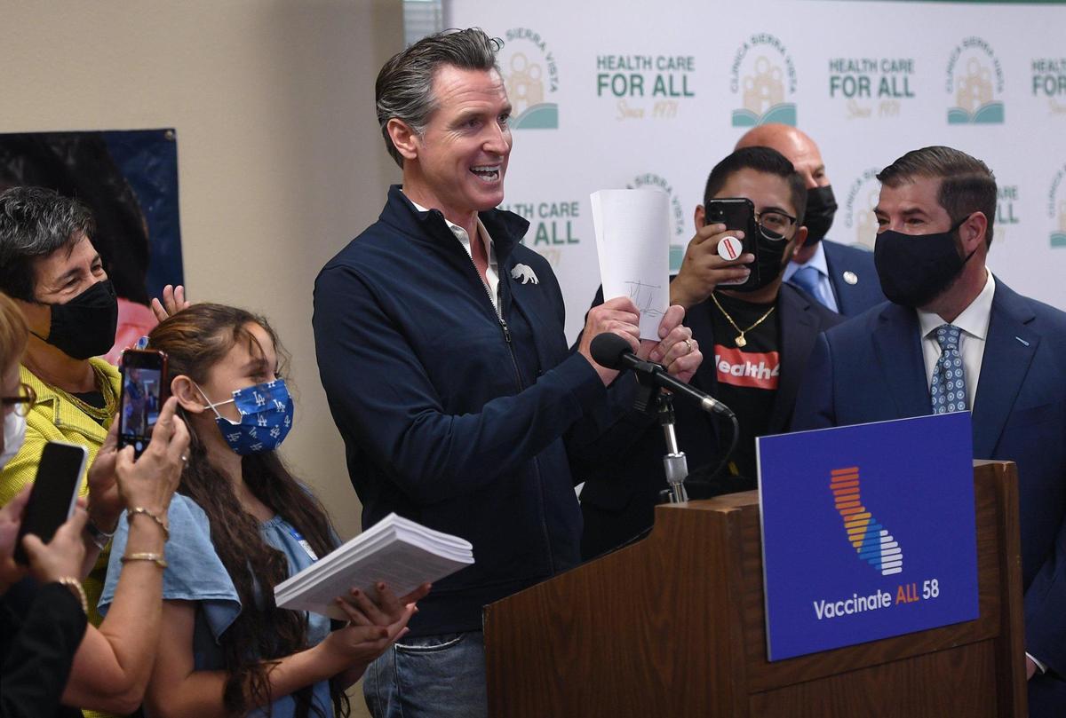 Gov. Gavin Newsom holds up paperwork after signing a bill expanding healthcare coverage for undocumented Californians in July 2021 at Clinica Sierra Vista in Fresno. Newsom further expanded Medi-Cal access in 2022.