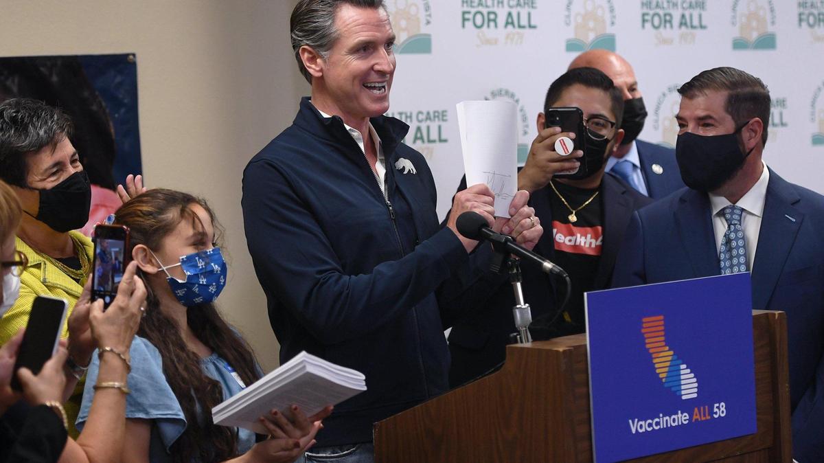 California Gov. Gavin Newsom, center, holds up the paperwork after signing a bill expanding health care coverage for undocumented Caifornians at Clinica Sierra Vista in 2021 in Fresno.