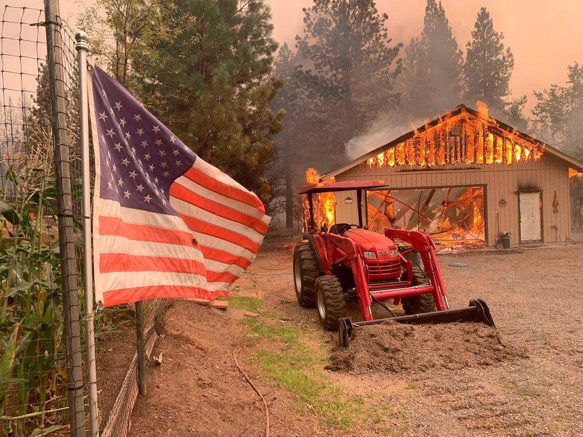 A tractor is left behind as a home burns outside Taylorsville in Plumas County, Calif., in the Dixie Fire on Friday, Aug. 13, 2021. The Dixie is the largest of 100 large fires burning in 14 states. The U.S. Forest Service said it has more than twice the number of firefighters working on the ground than at this point a year ago, and is facing “critical resources limitations.”