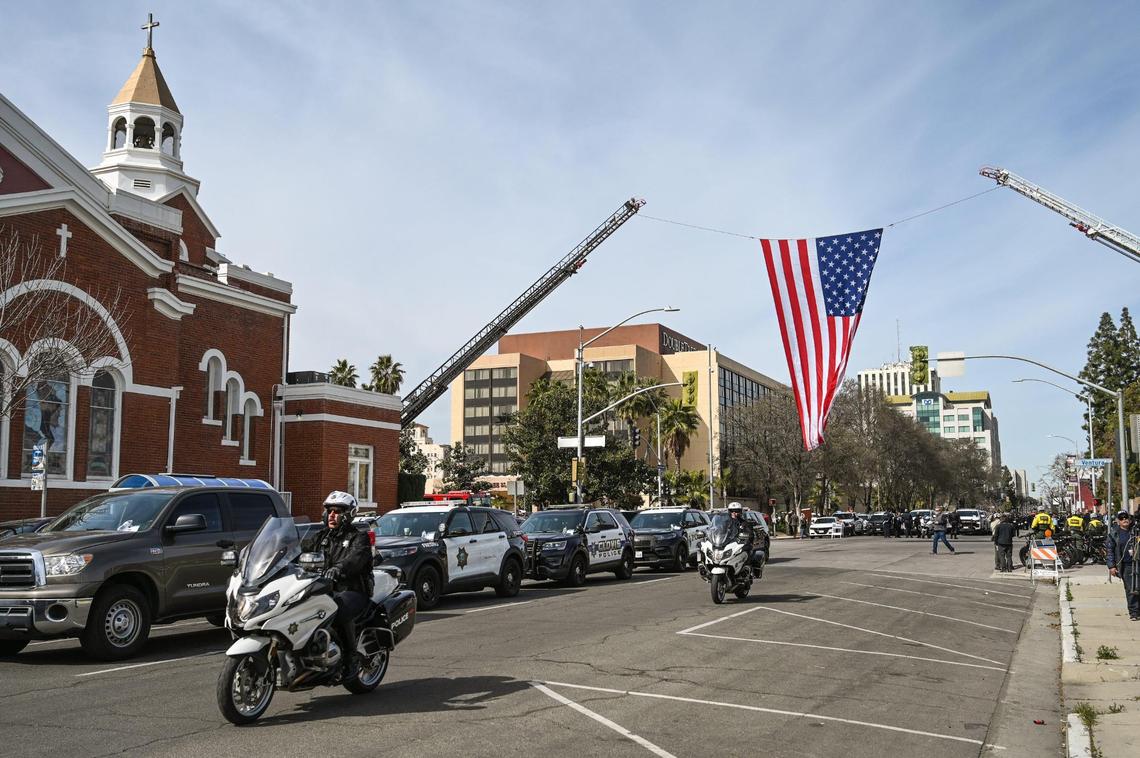 Fresno firefighters hang an American flag across M Street in downtown Fresno as officers from around the state begin lining up to escort fallen Selma officer Gonzalo Carrasco Jr. to Reedley for burial following his funeral service at Selland Arena on Thursday, Feb. 16, 2023.