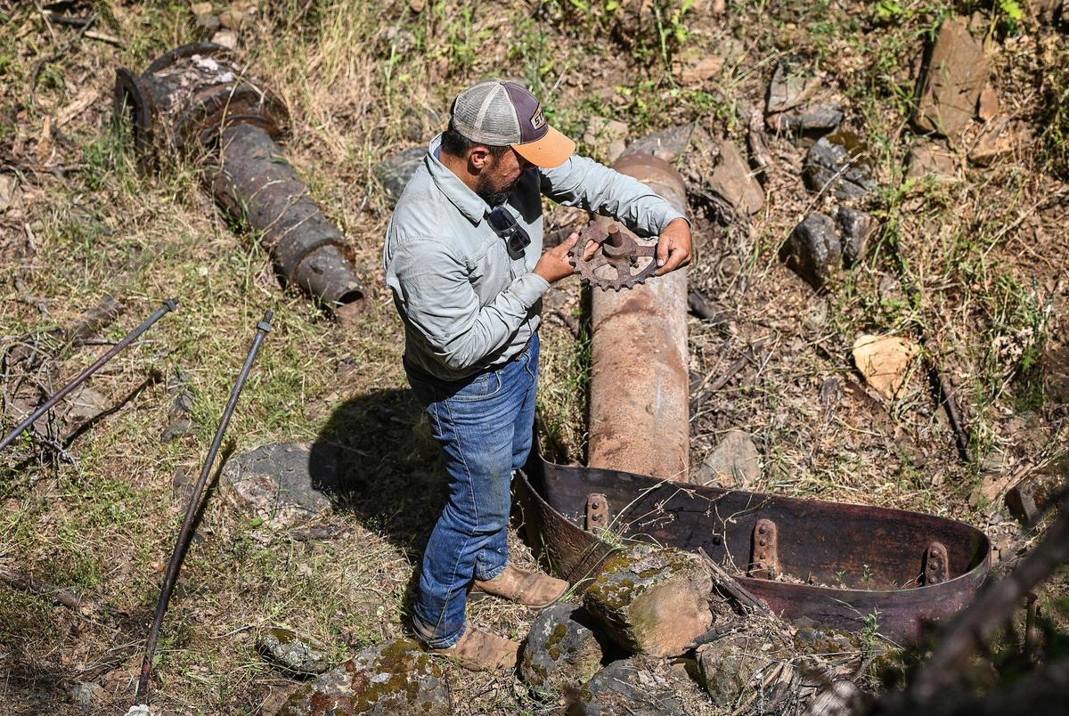 Sierra Foothill Conservancy land steward Jesus Garcia checks out an old gear piece left over from a Gold Rush era stamp mill near the Fresno River and the old Grub Gulch mining town off Road 600 in Madera County on Wednesday, May 27, 2022. The Wright Ranch was recently acquired as a conservation easement by the Sierra Foothill Conservancy.