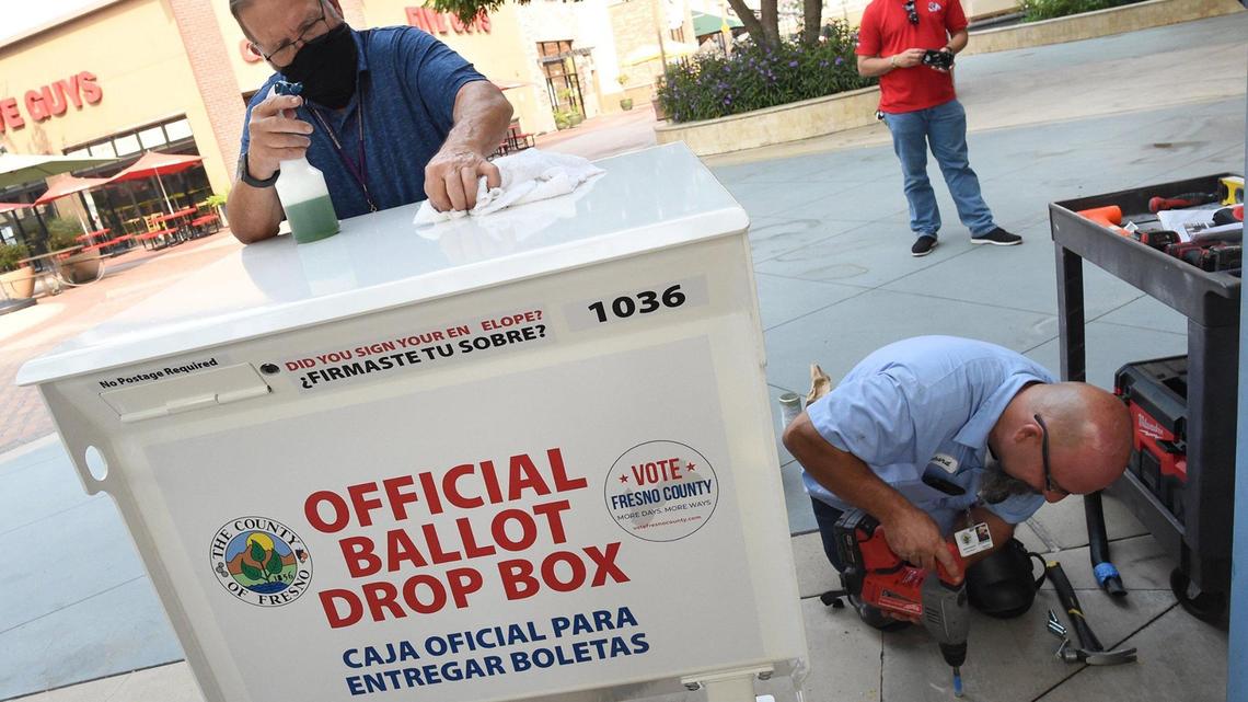 Russell Chappell, of the Fresno County Elections office, left, spruces up a ballot box as county maintenance worker Richard Rodgers, right, installs mounting hardware for the box being installed at River Park Shopping Center, Friday Oct. 2, 2020.