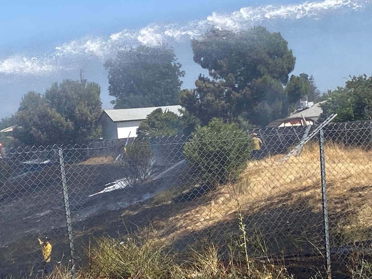Water is poured onto a burnt field after a grass fire kicked up and spread due to high winds that threatened homes in Fresno, California on Saturday, June 21, 2025.