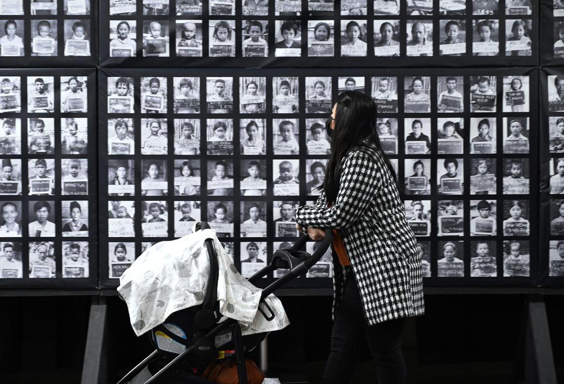 A visitor walks pas a wall of identification photos at Vinai, the Hmong Refugee Experience, a multimedia exhibit chronicling the Hmong community as they transitioned from their home country to refugee camps and finally the United States. The free exhibit is located in the Big Fresno Fair’s Commerce Building, is open now through to Jan. 1, 2023. Photographed Friday, Dec. 23, 2022 in Fresno.