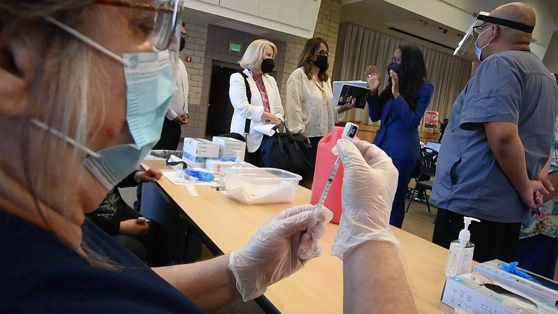 A vaccination tech draws a syringe of the Pfizer vaccine, as California Surgeon General, Dr. Nadine Burke Harris (second from right) is briefed upon her visit to the Covid-19 vaccination clinic at the  Kerman Community Center, June 9, 2021.