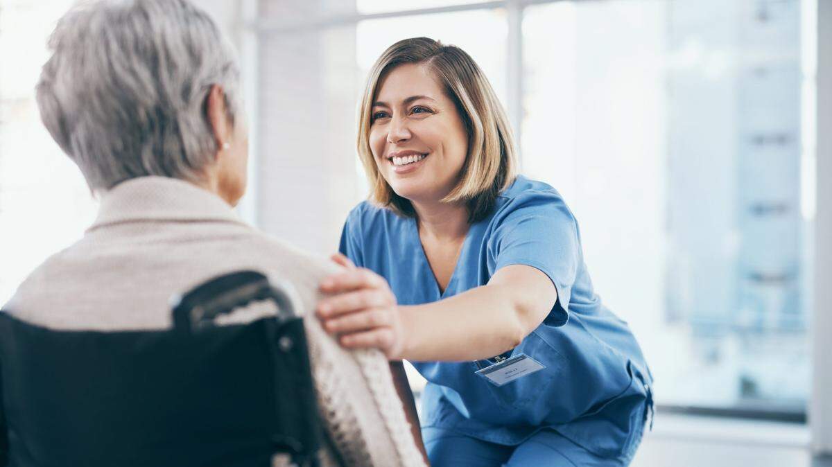 Nurse or caregiver taking care of a senior retired woman sitting on a wheelchair in a modern facility. Happy female healthcare professional consulting a mature lady and giving support