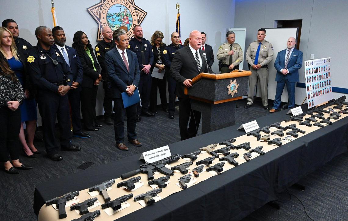 Fresno Mayor Jerry Dyer, center, stands speaking to the media at a joint press conference announcing the results of a 5-month long investigation into street gangs called No Fly Zone. Firearms confiscated during the operation are seen in the foreground. Photographed Friday, April 15, 2022 in Fresno.