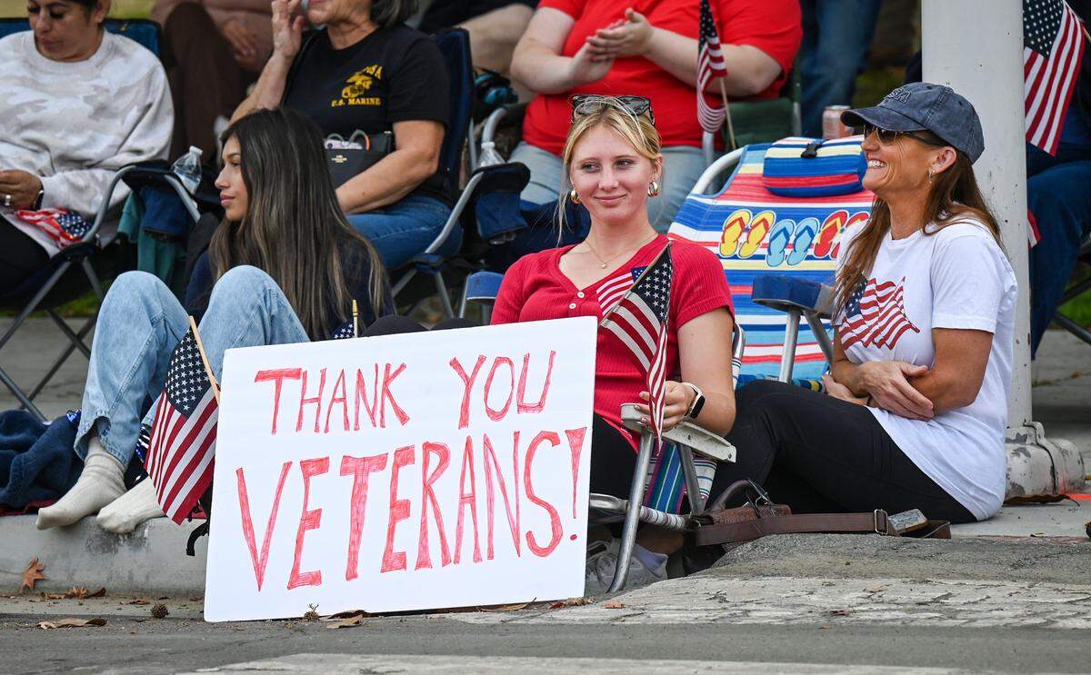 Parade-watchers sit near a sign thanking veterans during the Central Valley Veterans Day Parade in downtown Fresno on Tuesday, Nov. 11, 2025. 