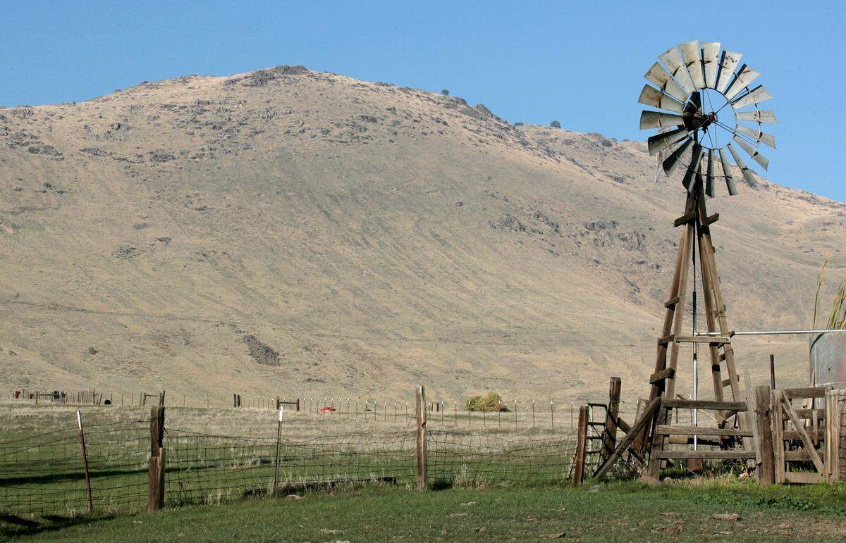 An old windmill stands in pasture land with Jesse Morrow Mountain, site of a proposed sand and gravel mine that drew widespread opposition in the early 2010s, in the background.