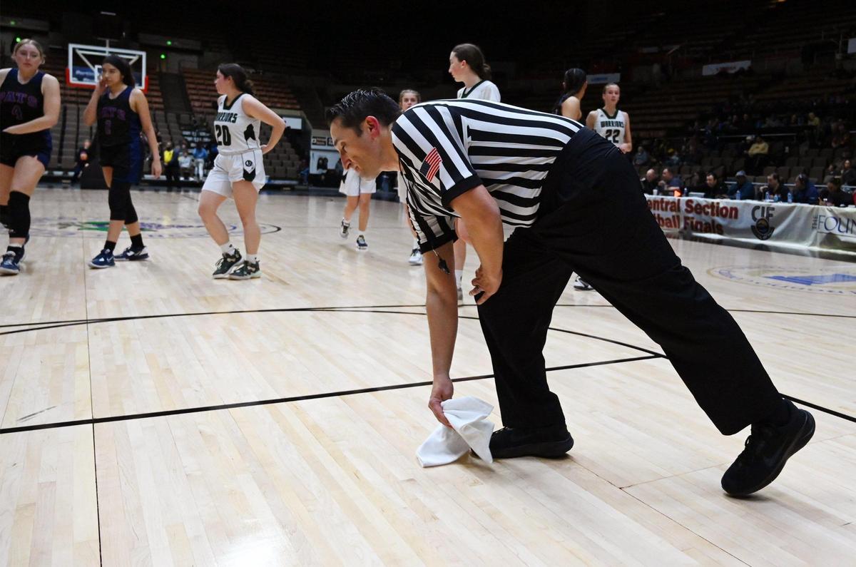 An official picks up a towel where water has been dropping on the Selland Arena court at the CIF Central Section basketball championships Friday, Feb. 24, 2023 in Fresno.