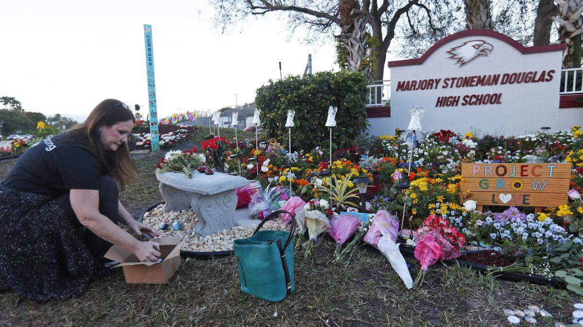 Suzanne Devine Clark, an art teacher at Deerfield Beach Elementary School, places painted stones at a memorial outside Marjory Stoneman Douglas High School during the one-year anniversary of the school shooting, Thursday, Feb. 14, 2019, in Parkland, Fla.
