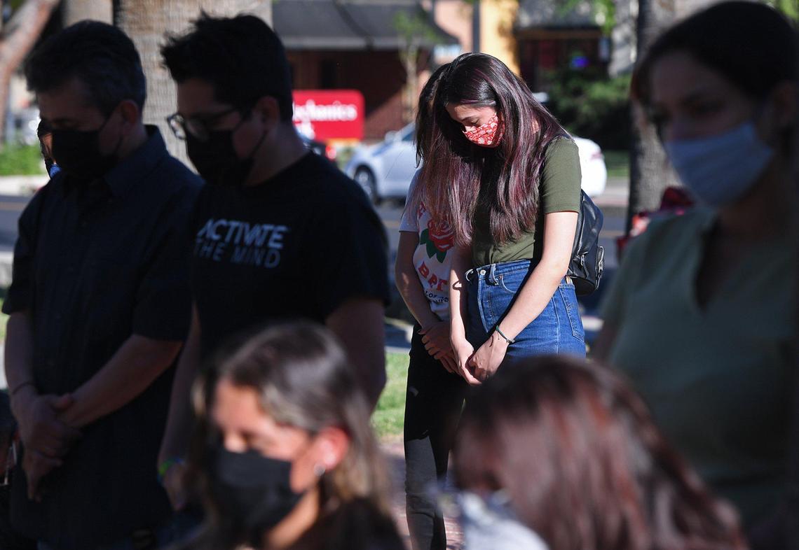 Karina Juarez from UC Merced, center, joins others in bowing their heads during an event on the steps of the old Kings County Courthouse in observance of essential workers who died from COVID-19 last year on Wednesday, April 28, 2021.