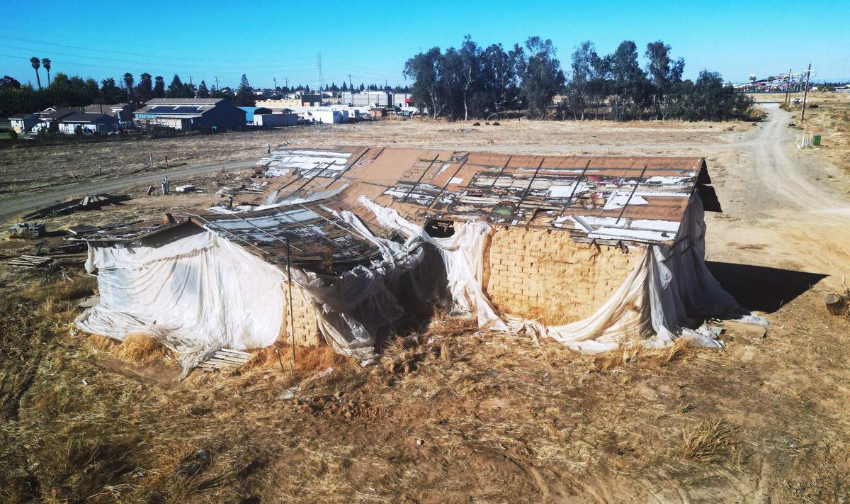 The historic Jose Garcia Adobe sits wrapped in tattered plastic on land south of Shaw Ave. within view of Island Waterpark just to the north, top right corner, photographed Tuesday, Nov. 28, 2023 in Fresno.
