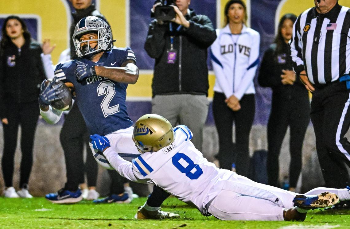 Clovis East’s Harold Duvall, left, stretches for an extra yard after catching a deep throw for a first down as he’s pulled down by Clovis’ Dezjour Malone during their Central Section Division 1-AA semifinal game at Lamonica Stadium in Clovis on Friday, Nov. 15, 2024.