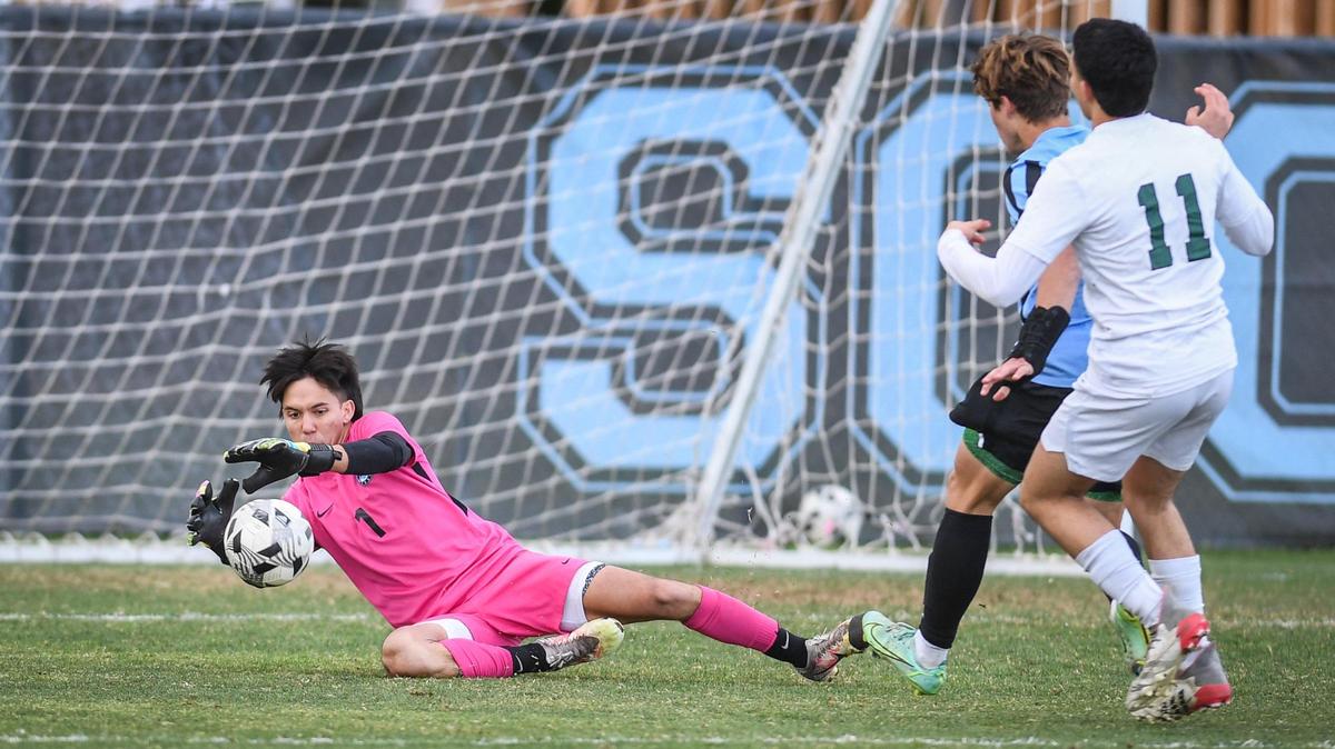 Clovis North goalkeeper Lucas Tabangcura dives on the ball on a scoring attempt by Reedley’s Levy Alcantar, right, during their match at Clovis North on Tuesday, Feb. 22, 2022.